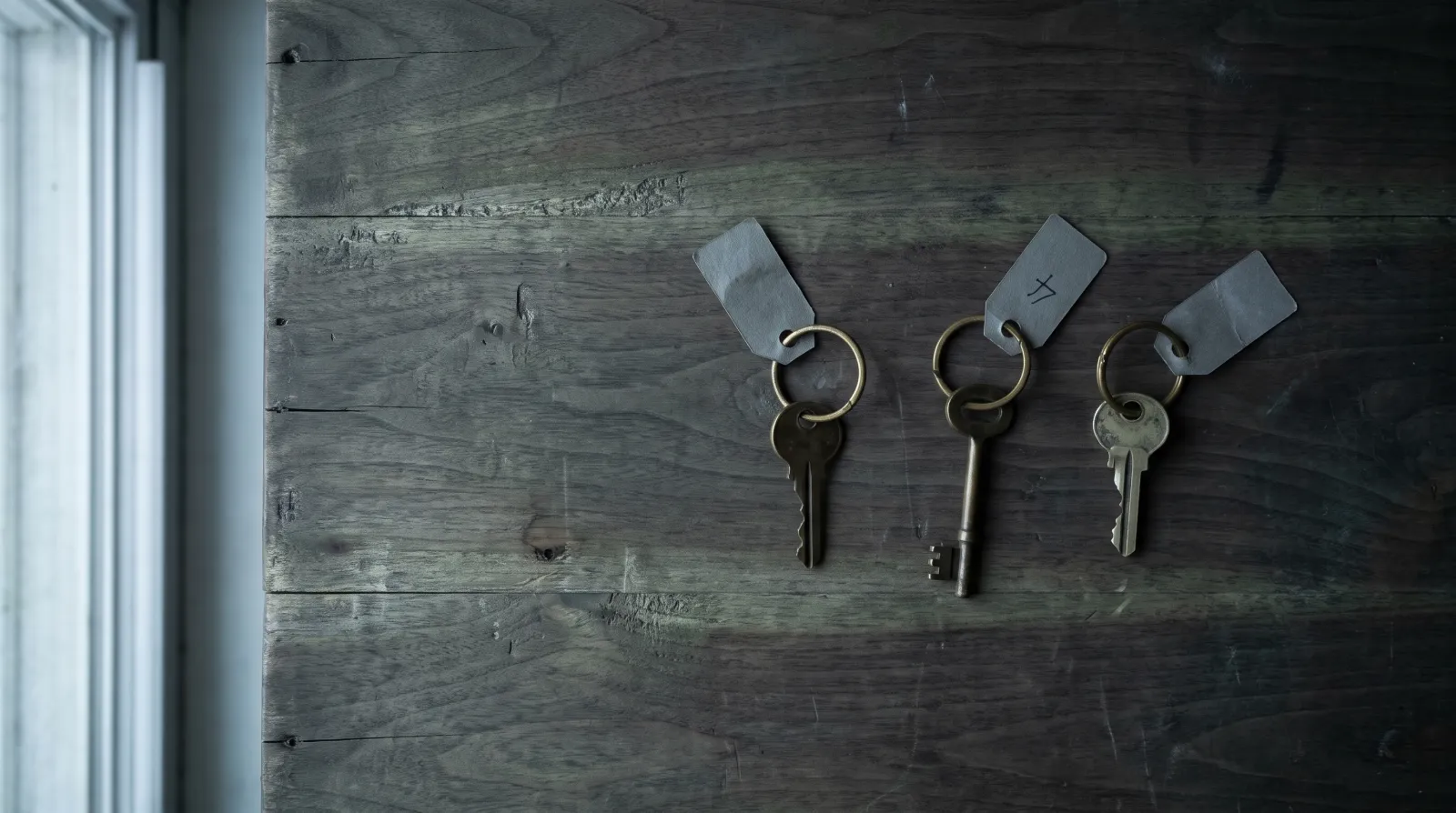 Illustrative overhead photograph of three brass keys and paper tags on stained wood